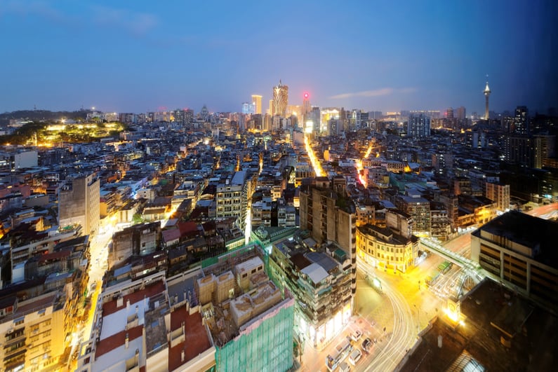 Urban skyline of vibrant Macao City in blue twilight, with the famous landmark Macau Tower (Convention & Entertainment Center) and Grand Lisboa Hotel & Casino standing amid crowded buildings at dusk