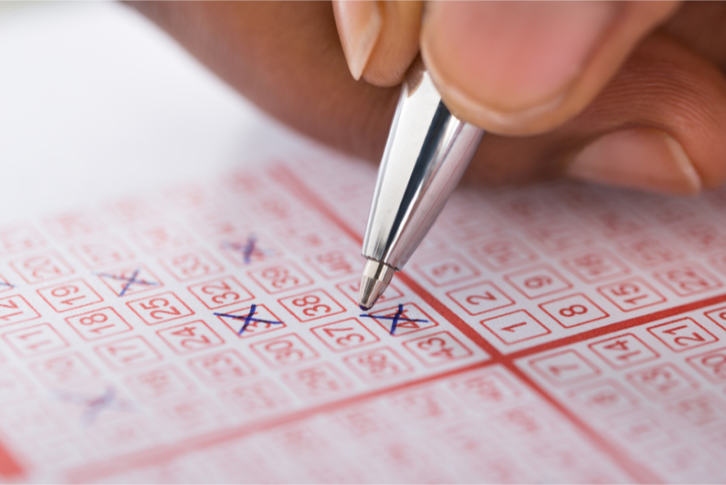 Close-up Of Person's Hand Marking Number On Lottery Ticket With Pen